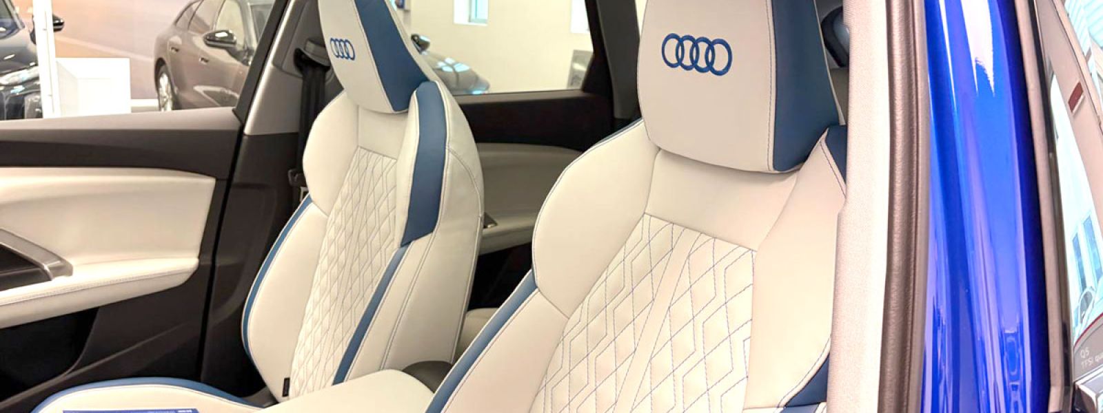 sedili anteriori auto bianchi con bordi e cuciture blu e logo Audi blu ricamato sul poggiatesta