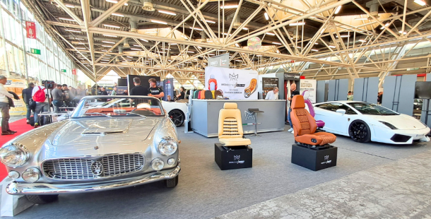 stand fieristico con esposizione a sinistra di un'auto d'epoca, al centro 3 sedili con diverse lavorazioni e a destra un'auto sportiva